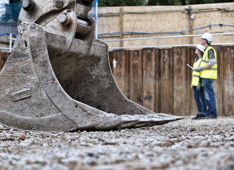 Two workers on a construction site with excavator in foreground