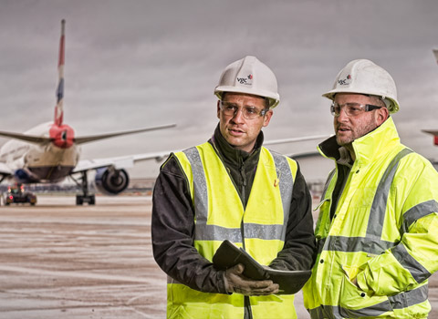 Two workers on the apron with airplanes in the background at Heathrow Airport, London