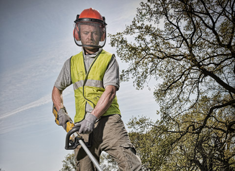 Gardener using a DeWalt strimmer in a park in London