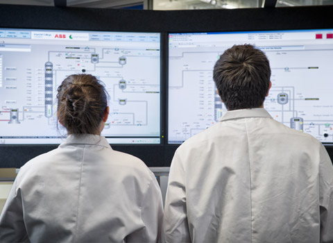 Two people in white coats looking at large computer screens