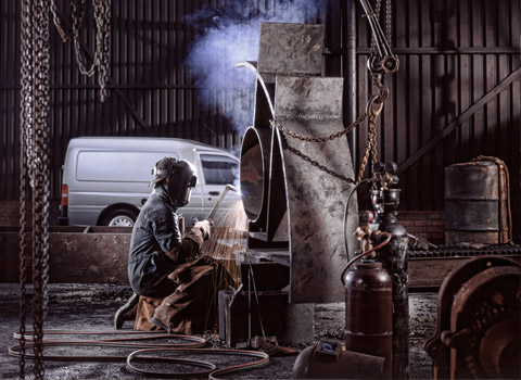 Welder working on metal with van in background